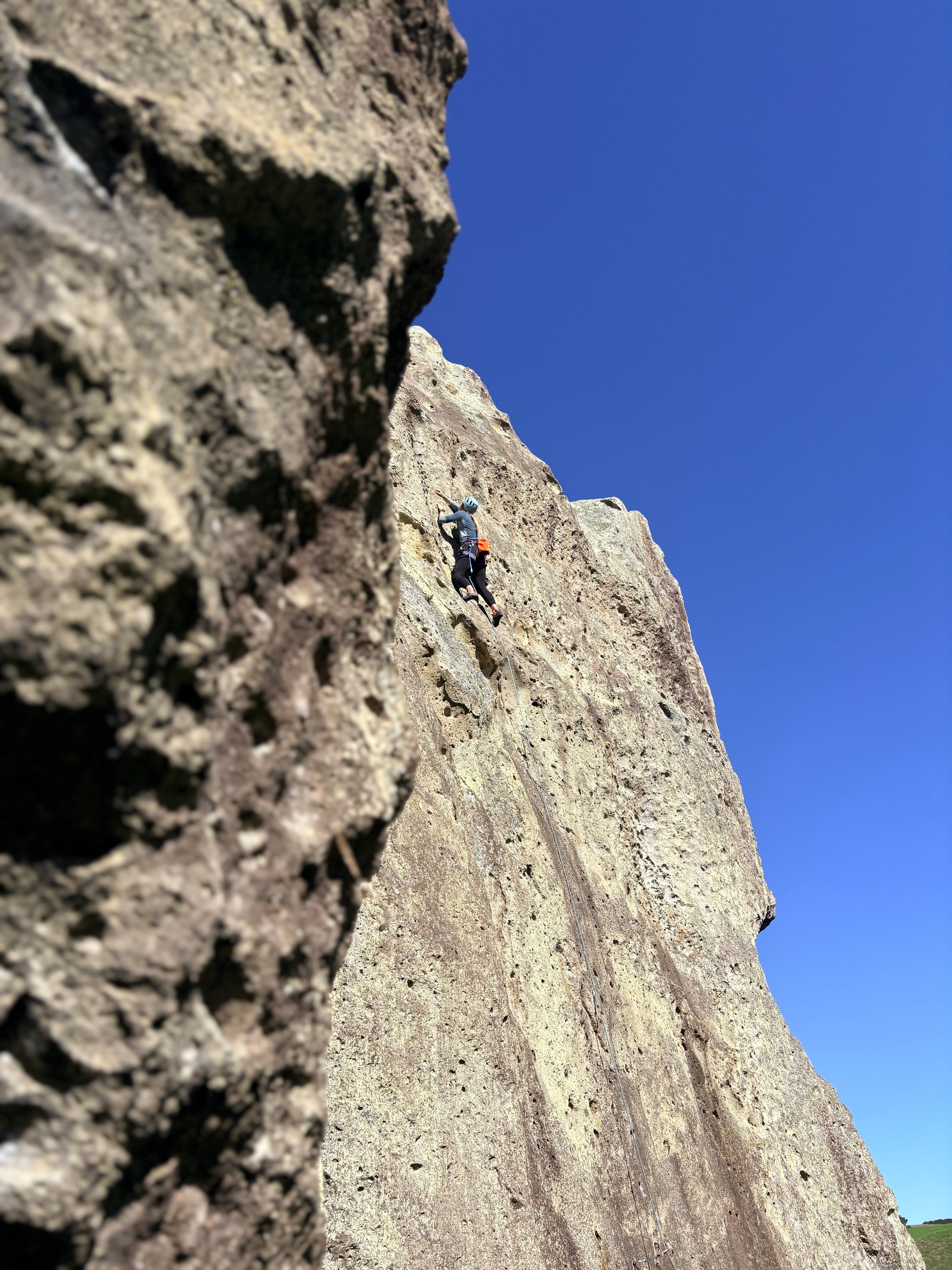 A rock climber is shown scaling a steep, textured rock face under a clear blue sky.