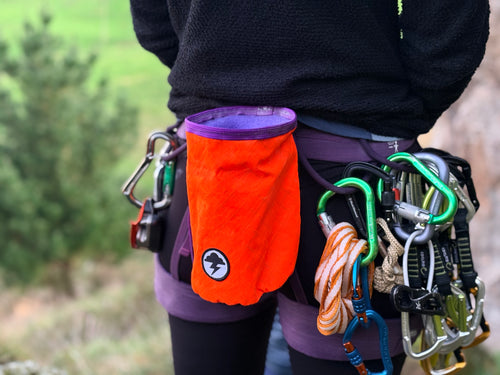Person wearing a climbing harness with orange chalk bag and various climbing equipment.